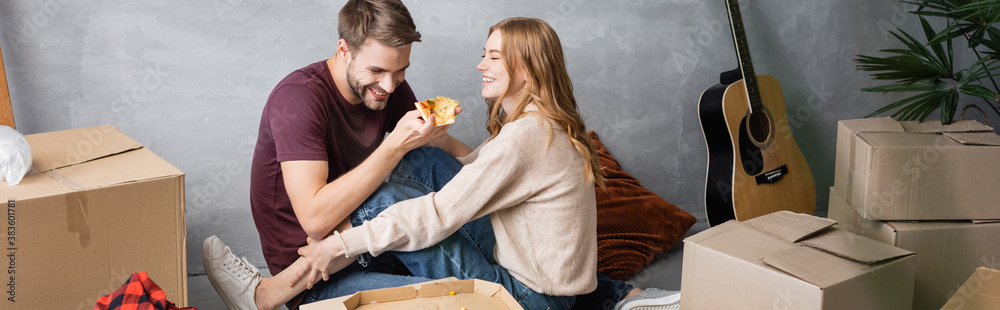 panoramic crop of pleased man holding pizza near woman and carton boxes panoramic crop of pleased man holding pizza near woman and carton boxes
