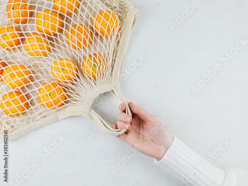tangerines and female hand
A female hand holds a cotton mesh with tangerines in a diogonal fashion on a white cement background, close-up top view. photo