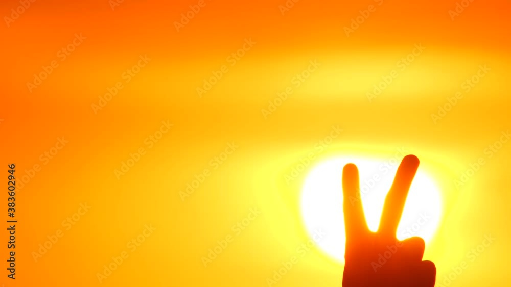 V sign is showed by man hand on a beautiful orange sunset or sunrise background. The symbol of Victory. Victory over a virus. Shaped hand of the letter V. A New Beginning. V sign is showed by man hand on a beautiful orange sunset or sunrise background. The symbol of Victory. Victory over a virus. Shaped hand of the letter V. A New Beginning.