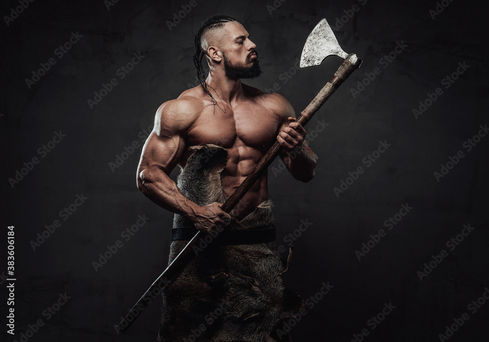 Nord muscular fighter with dreadlocks and beard posing looking at his axe which he holding on hands in dark background.