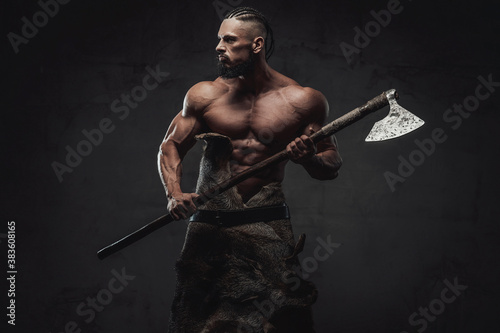 Fototapeta Furious and bearded viking warrior with naked torso and huge biceps prepared to fight holding his weapon in dark background