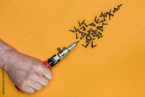 male hand holds a screwdriver on a yellow background. A scattering of black screws. flat lay for construction tools concept. Top view