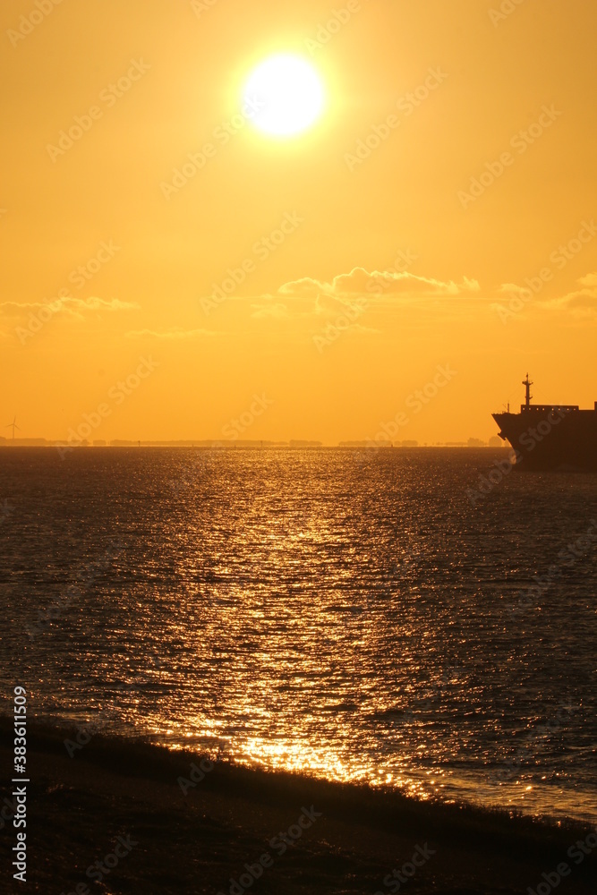 a beautiful sunset at the westerschelde sea with an orange sky above the black water and the nose of a ship at the right