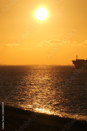 a beautiful sunset at the westerschelde sea with an orange sky above the black water and the nose of a ship at the right