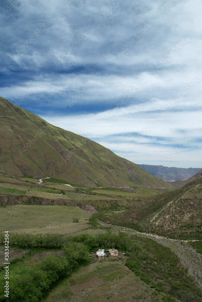 The green valley and hills. View of a small farm house in the rural field surrounded by mountains.