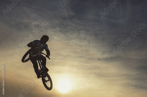 Unrecognizable biker performing acrobatic jump at sunny sky - Guy riding bmx bicycle at extreme sport competition on sunny afternoon - Alternative lifestyle concept on warm sunshine colors. Warm toned