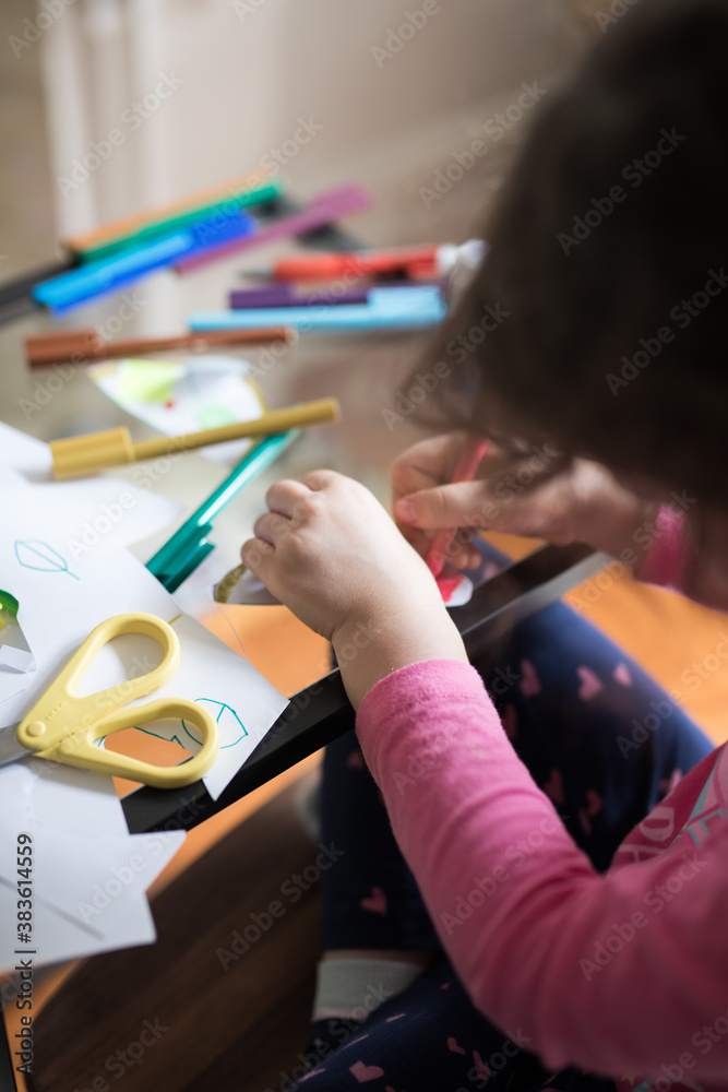 Looking down at a young girl child seated at her study desk learning school from home with ipad tablet education program colored colorful textas scissors glue Looking down at a young girl child seated at her study desk learning school from home with ipad tablet education program colored colorful textas scissors glue