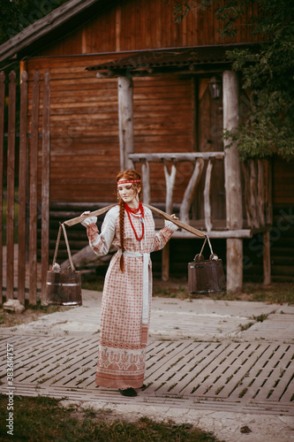 Beautiful Slavic girl with long blonde hair and brown eyes in a white and red embroidered suit and a yoke on her shoulders.Traditional clothing of the Ukrainian region. © Aleksei Zakharov