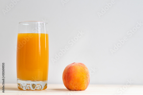 Close up of a glass of fresh peach juice and a ripe juicy peach. Copy space with place for text.