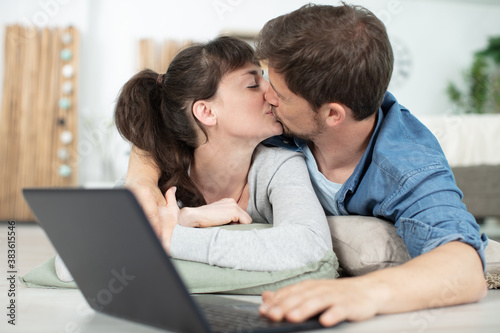 happy young couple kissing next to laptop