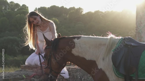 Woman gently touhing and caressing a horse in the forest at sunset. Dreamy look video of a female interacting with a horse in the wild. Lovely moment between human and animal in nature photo