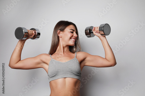 Workout time. Young woman doing exercise at home, smiling and posing over white wall.