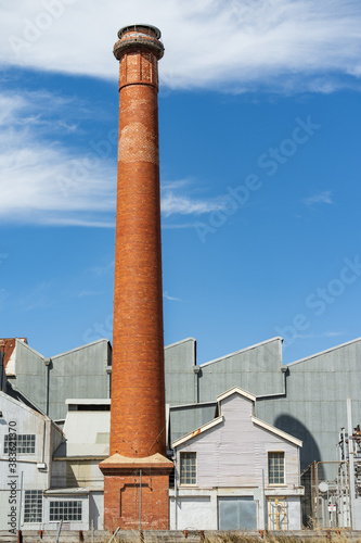 A tall brick chimney beside a large tin factory photo