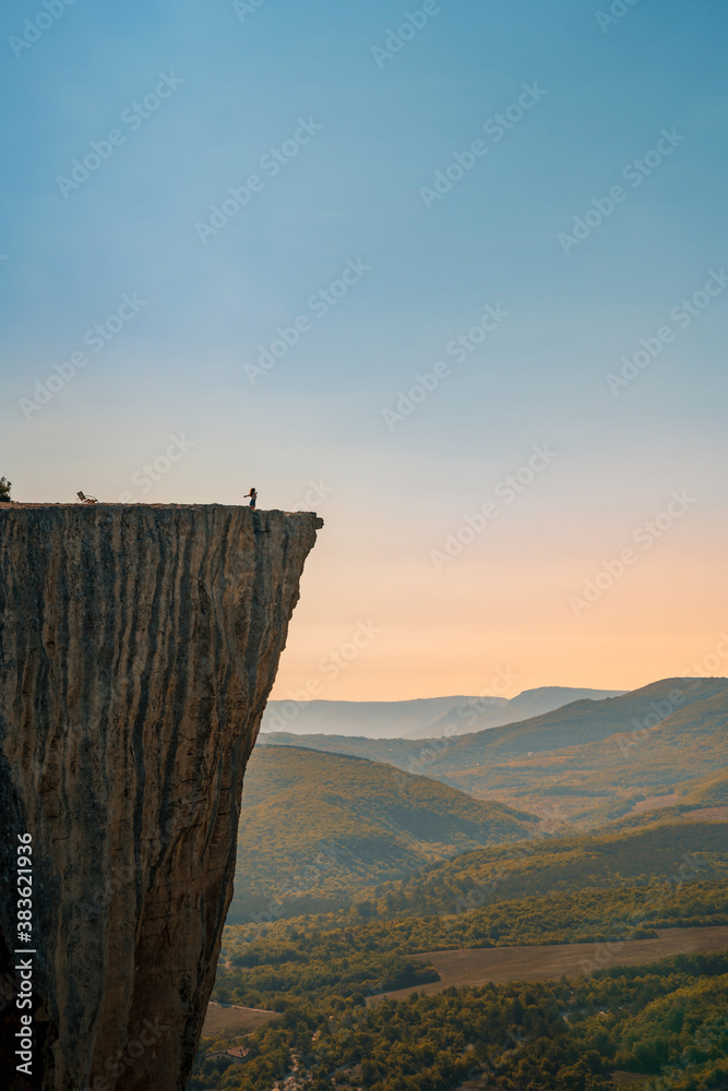 A small figure of a woman tourist standing on the edge of a cliff in the summer mountains. The concept of a small man in the midst of a powerful nature.