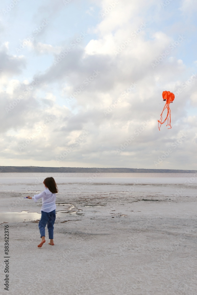 girl running on pink salt lake with orange kite
