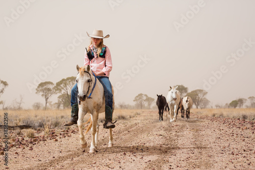 Teenage girl riding pony on dirt road with horses following her photo