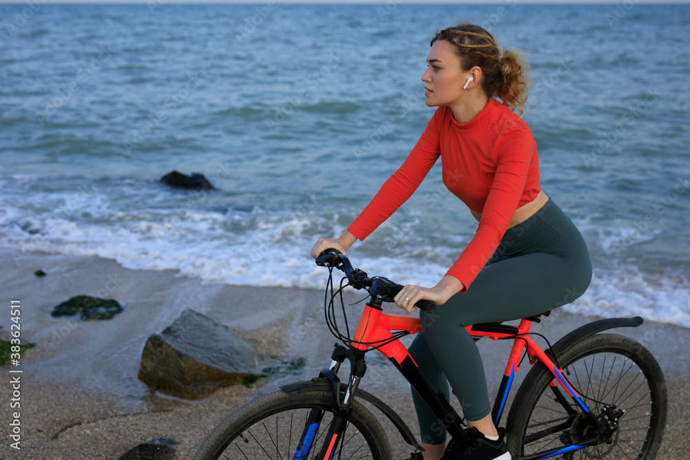 Fototapeta premium Young woman in orange t-shirt with bicycle on the sea beach