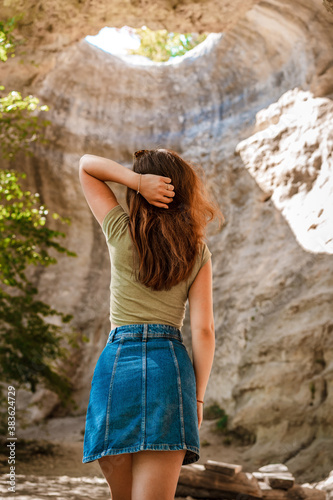 Rear view of a young woman adventurer standing in an underground cave with an opening to the outside, Sunlight through a cave