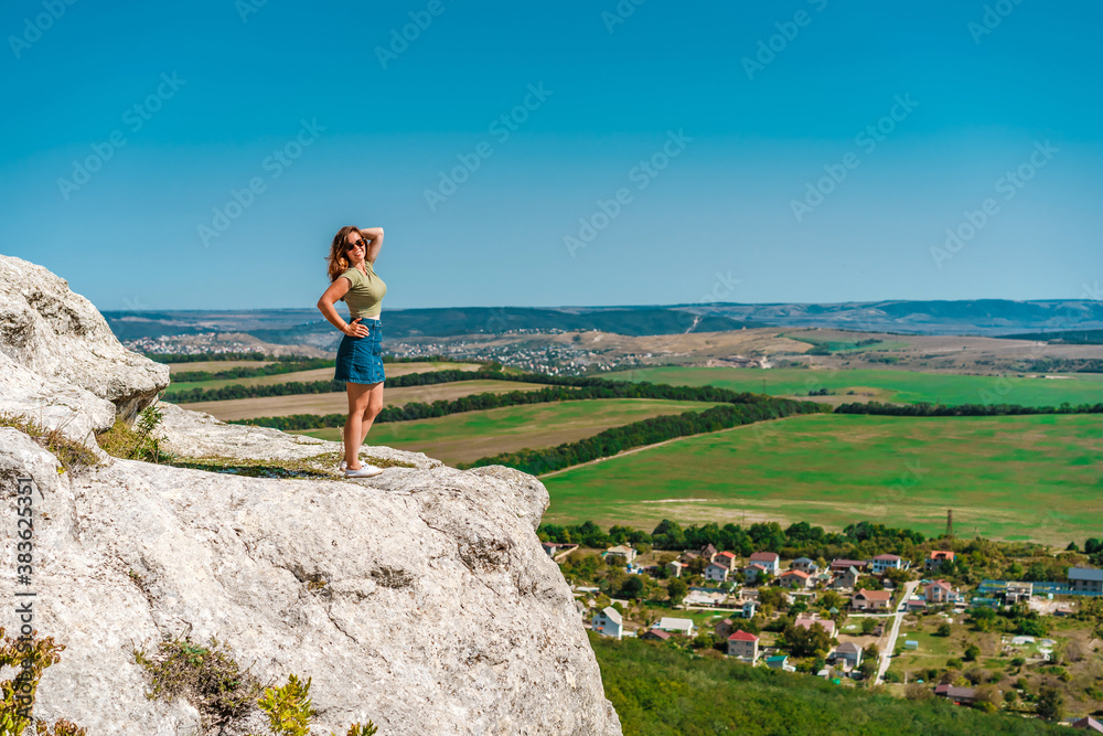 A young woman stands on a rock overlooking a green valley