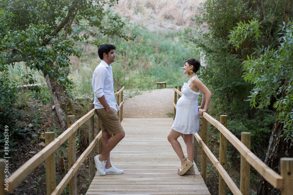 Naklejka premium Couple of pregnant woman and man, walking on a wooden bridge in the countryside. Maternity.