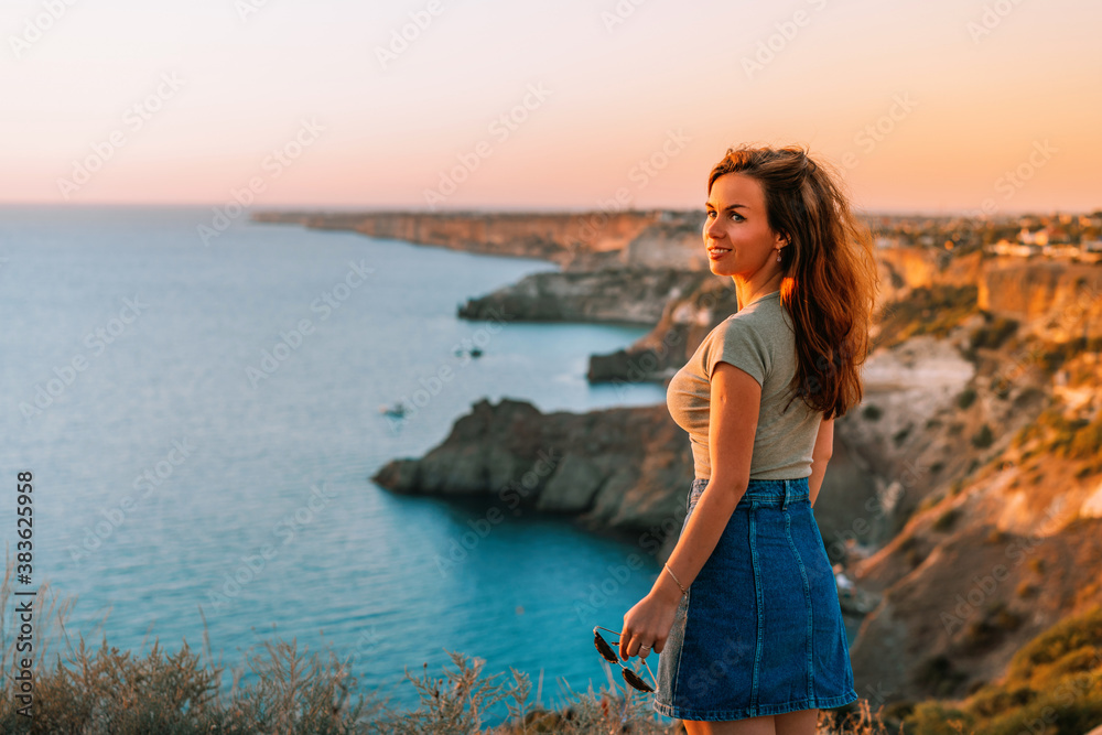 Attractive young woman posing against the blue sea and mountains at sunset. The concept of romance, travel and tourism Attractive young woman posing against the blue sea and mountains at sunset. The concept of romance, travel and tourism