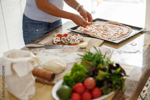 Fototapeta Naklejka Na Ścianę i Meble -  Beautiful smily handsome woman is preparing tasty fresh italian pizzawith vegetables at her kitchen at home
