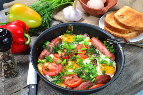 Scrambled eggs with fried sausages, onions, sweet red peppers, all in a frying pan.