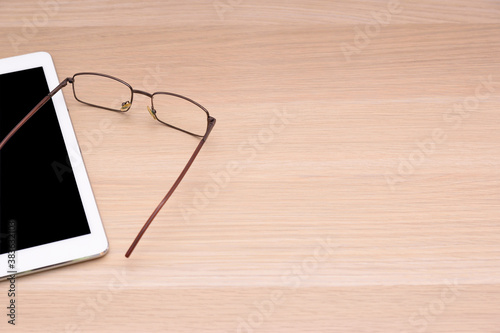 Glasses and tablet lying on a wooden table surface.