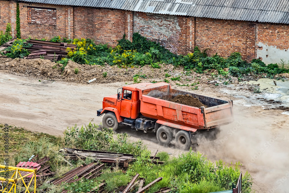 Red dump truck loaded with soil on construction site rides at high speed.