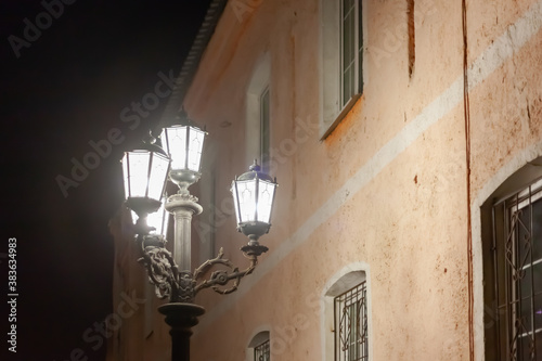 old street lamp shines at night against the backdrop of an old yellow building