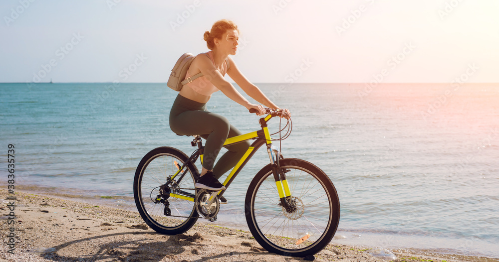Fototapeta premium Young woman bicycling along a beach