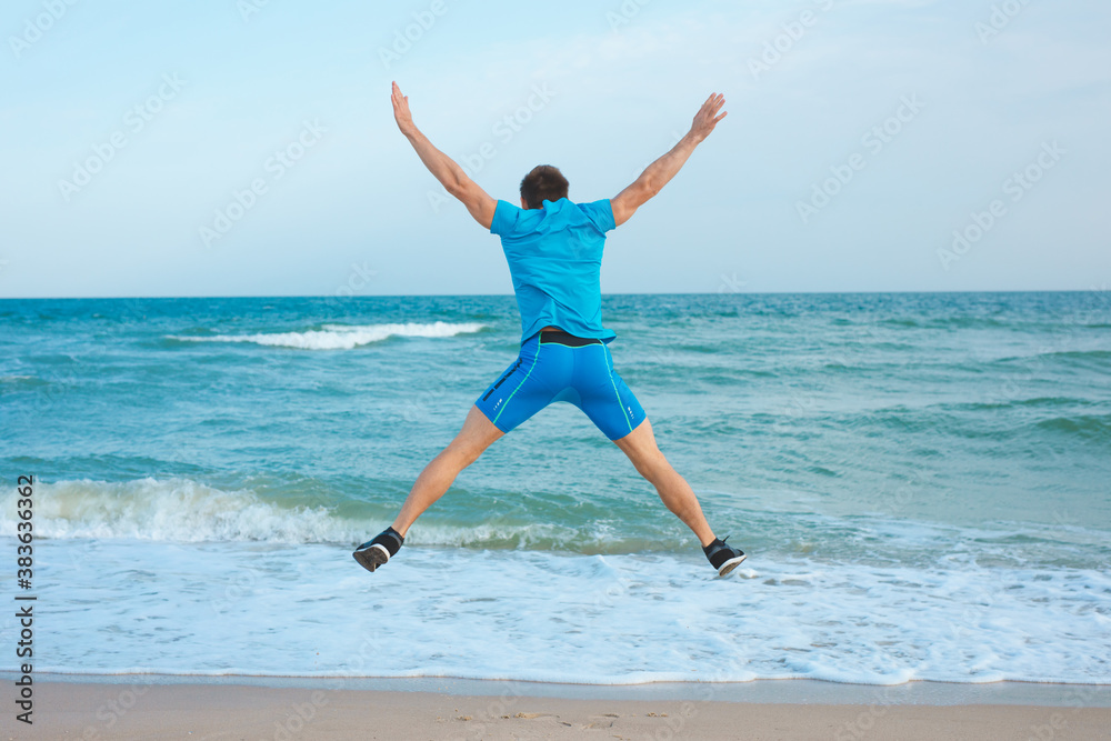 Happy man with raised hands jump on the sea, back view
