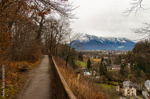 autumn park scenic view lonely empty trail path way under bare branches and near orange falling leaves with soft focus Alps mountain background landscape