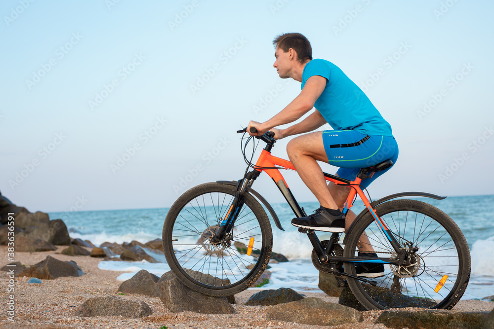 Fototapeta premium Young man bicycling along a beach