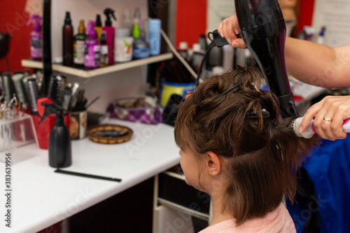 Beautiful teen girl at the hairdresser blow drying her hair after cutting it