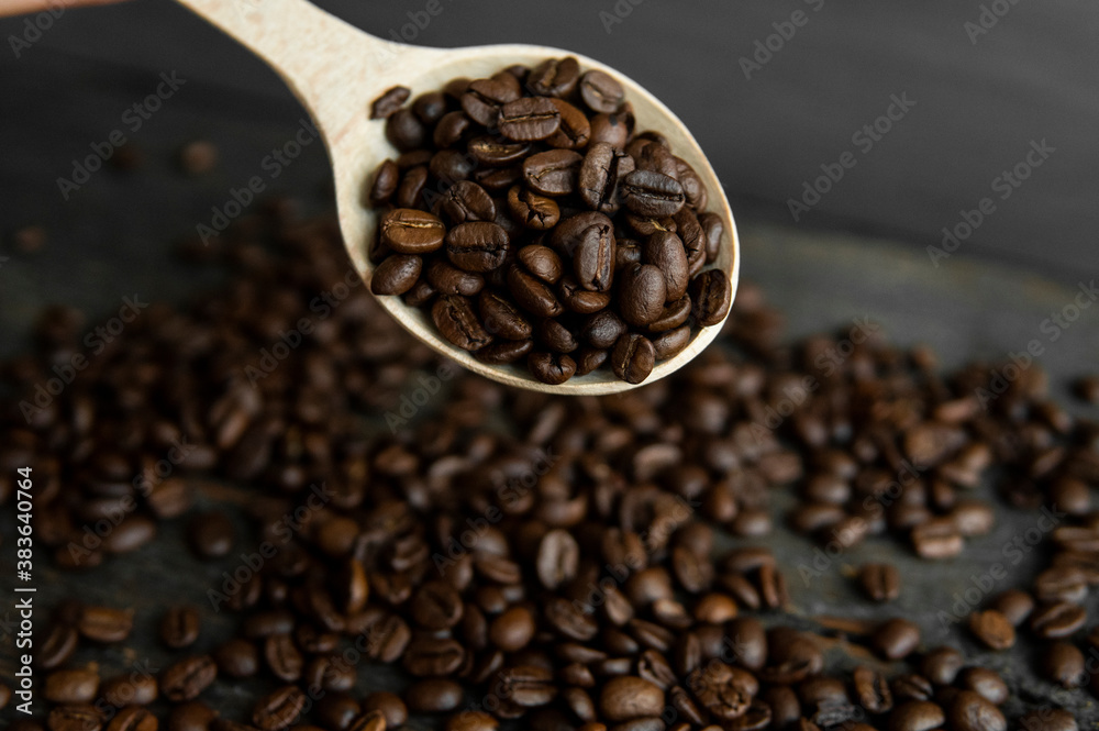 Fototapeta premium Fresh roasted arabica coffee beans in a wooden spoon and scattered coffee beans on a wooden table.