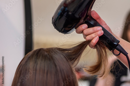 Beautiful teen girl at the hairdresser blow drying her hair after cutting it