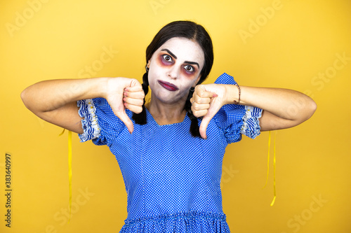 woman wearing a scary doll halloween costume over yellow background with angry face, negative sign showing dislike with thumbs down