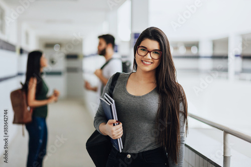 Portrait of young Brazilian student with backpack carrying books in college. photo