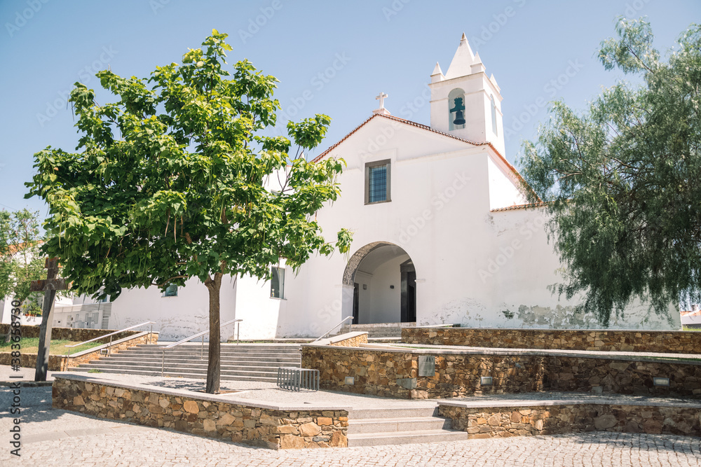 Fototapeta premium beautiful landscape of a small church built of white stone. little tree growing in front of the church. church in portugal. church with a tower with bells