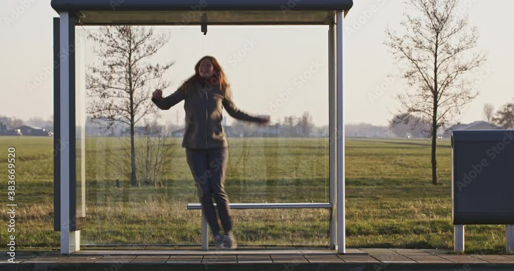 Woman jumping around at a remote countryside bus stop.