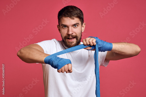 man in white t-shirt ties his hand with a bandage martial arts pink background