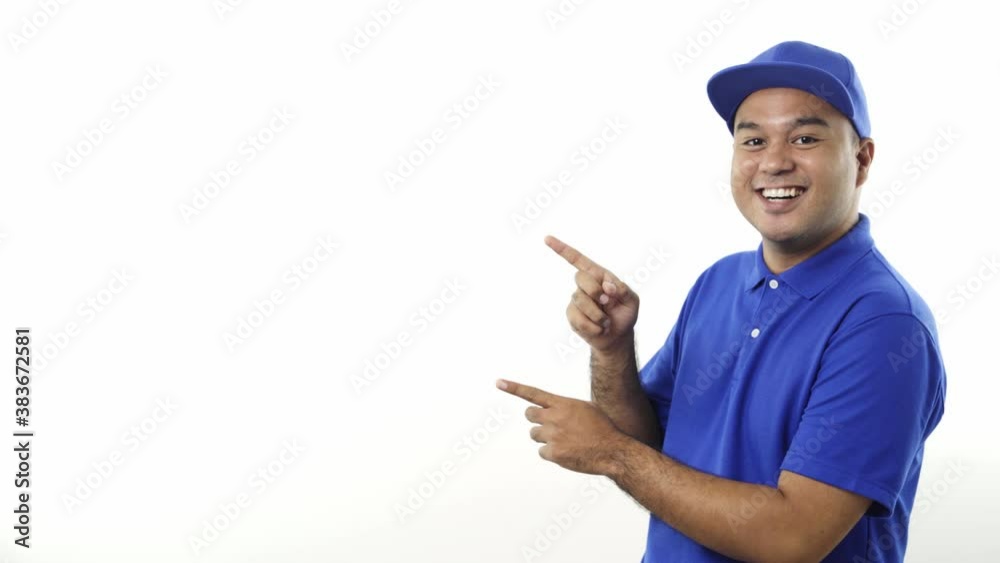 Smiling young asian delivery man in blue uniform pointing the finger to blank space for text on isolated white background. 4k Resolution. Smiling young asian delivery man in blue uniform pointing the finger to blank space for text on isolated white background. 4k Resolution.