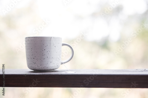 White simple ceramic herbal tea coffee mug herbal tea on a timber ledge outdoors against the blurred forest and trees natural background