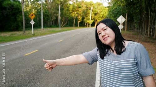 Asia woman hitchhiking on a sunny forest road. Tourist girl looking for ride to start her journey