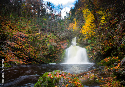 Foto Gushing water fall in an autumn forest landscape with dense trees, Cape Breton
