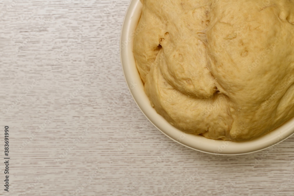 The puffed yeast dough rose in a light, large, round bowl. Fragment at the top right, on the table top. The puffed yeast dough rose in a light, large, round bowl. Fragment at the top right, on the table top.