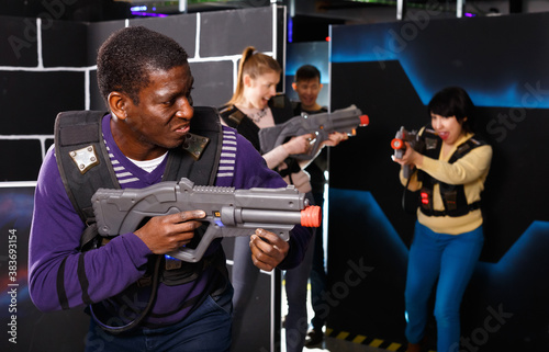 Portrait of cheerful smiling African-American with laser gun having fun on dark laser tag arena