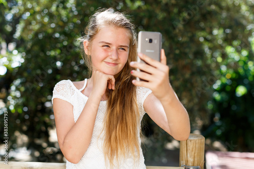 Portrait of teenage cute girl making photo with smartphone at sunny day outdoor