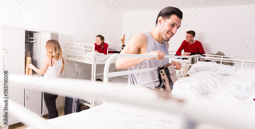 Man traveler staying in hostel, getting up to top bunk of two-story bed for sleep photo